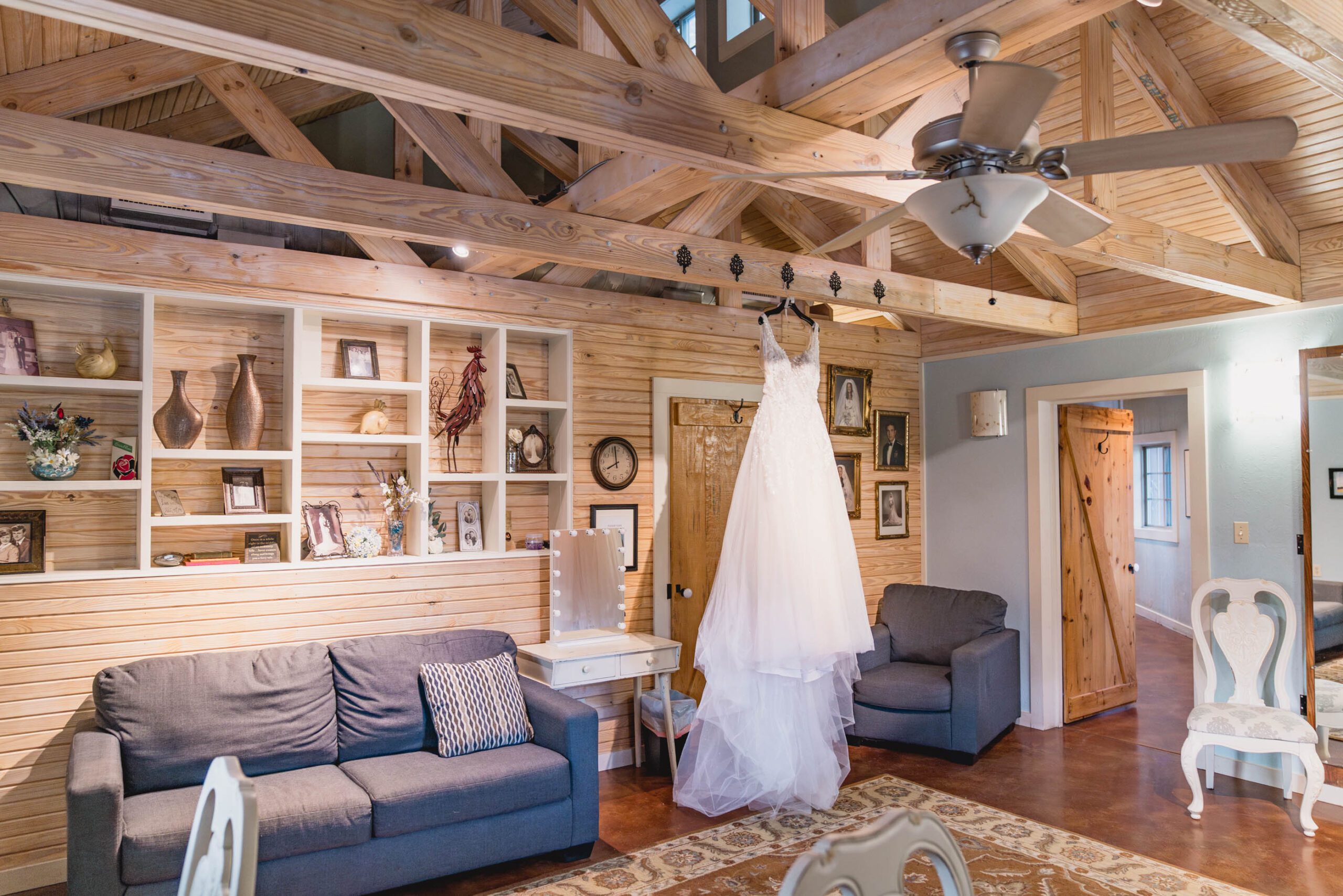 Brides Room at Hollow Hill Event Center Wedding and Event Venue, Weatherford, Texas. Room with pine walls and ceiling, sofa, chair, and vanity table. Wedding dress handing from rafter.